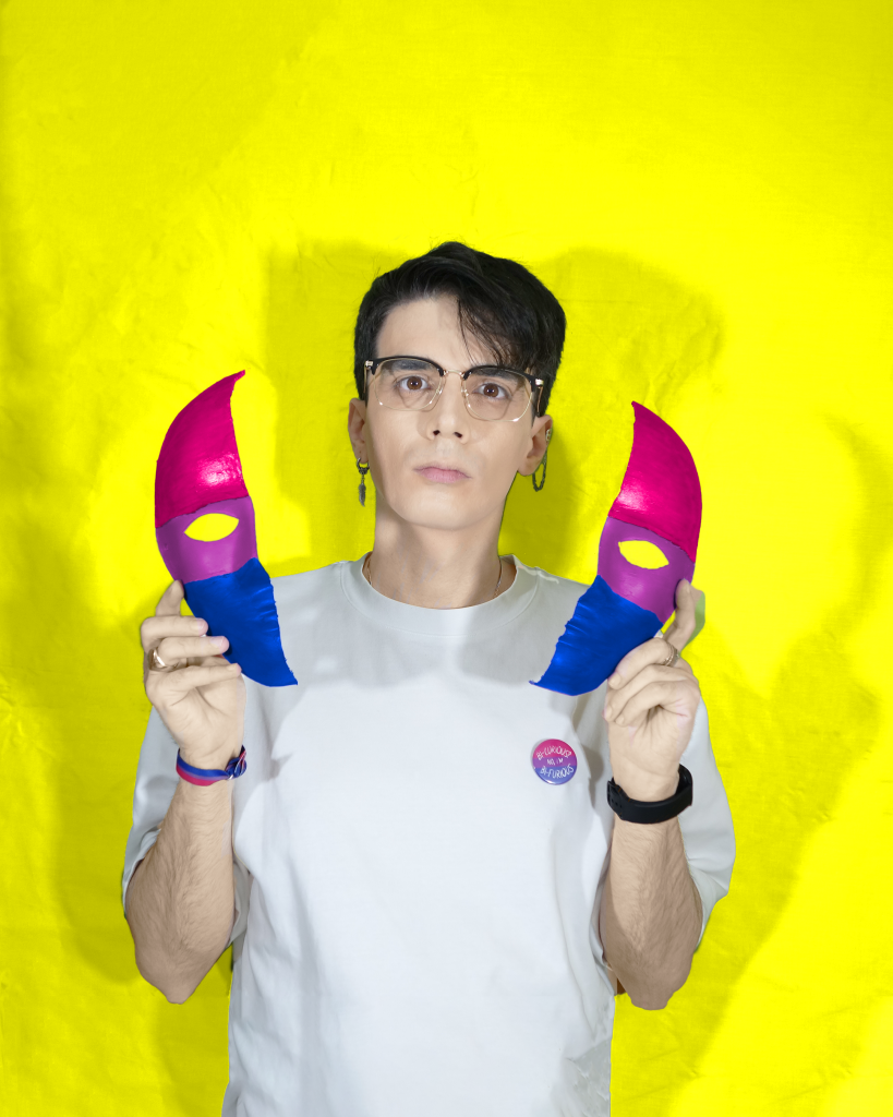 Alex Robles quitándose una máscara partida con la bandera de la bisexualidad